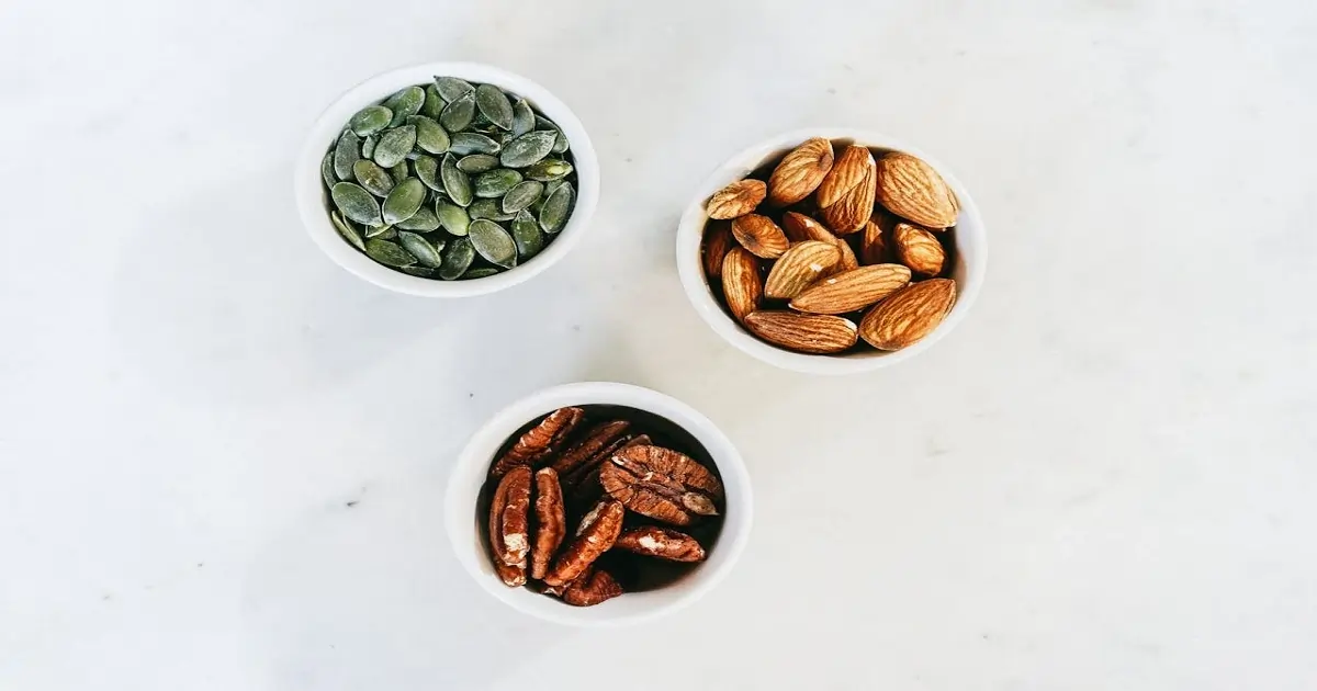Small bowls of almonds, pecans, and pumpkin seeds showing energy-dense foods