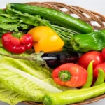Assorted fresh vegetables including lettuce, bell peppers, cucumber, tomato, and eggplant in a basket