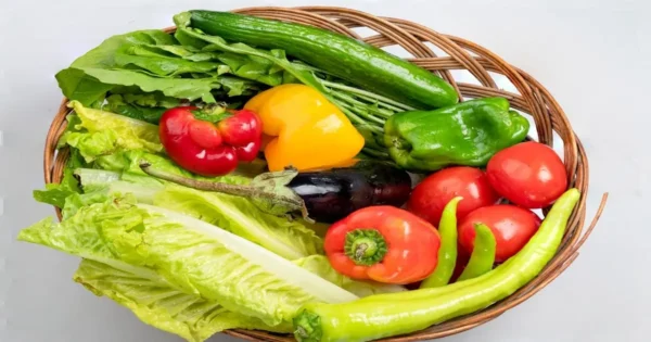 Assorted fresh vegetables including lettuce, bell peppers, cucumber, tomato, and eggplant in a basket